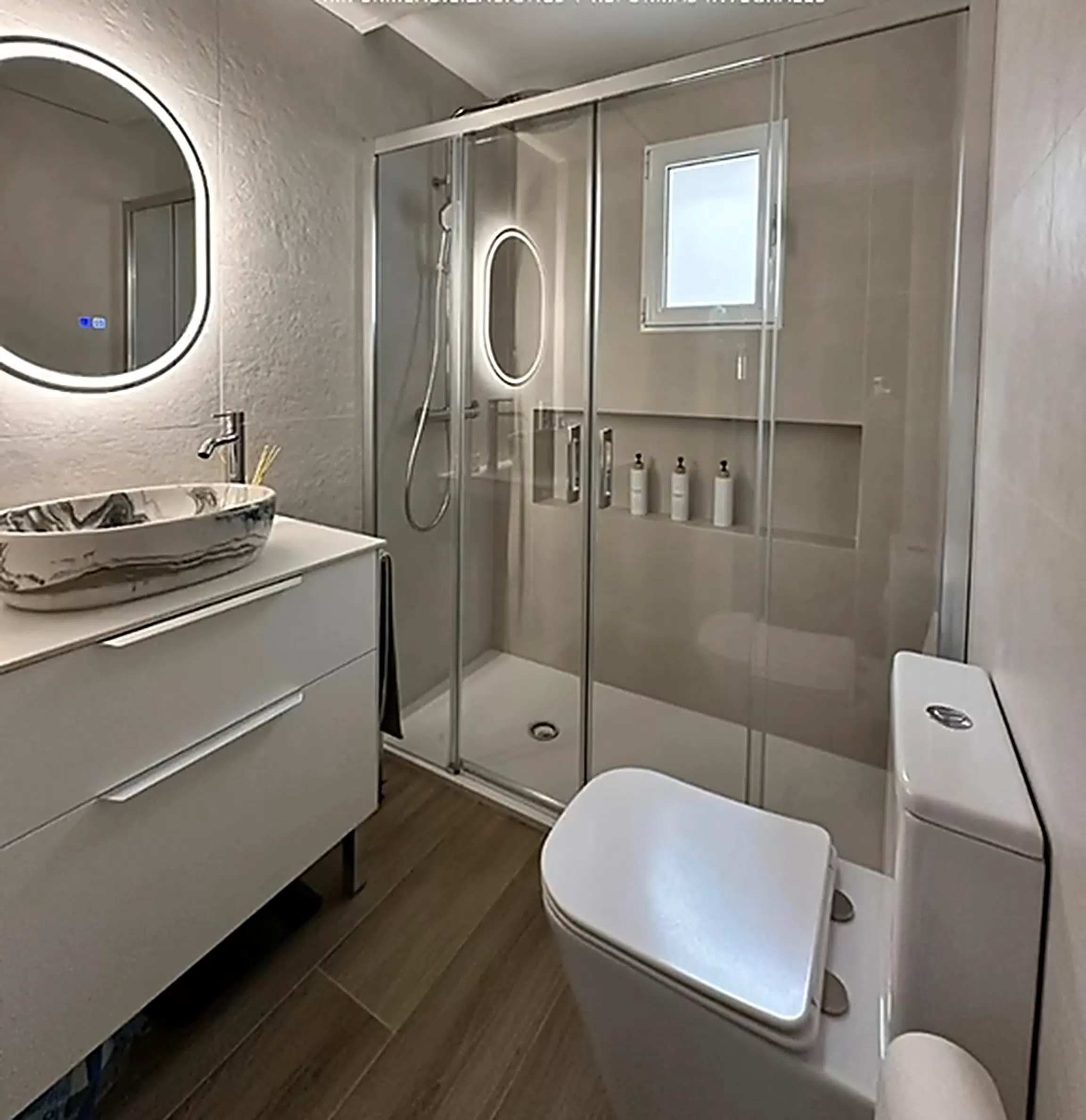 Baño terminado con ducha, mampara y espejo redondo retroiluminado
